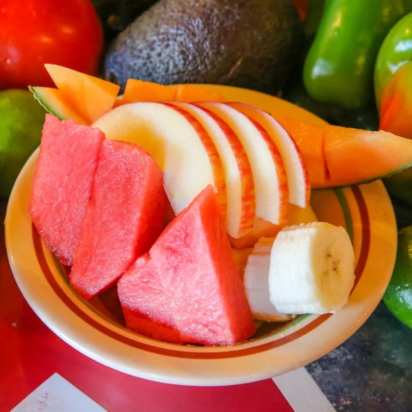 A colorful fruit plate with watermelon, sliced apples, cantaloupe, and banana slices.