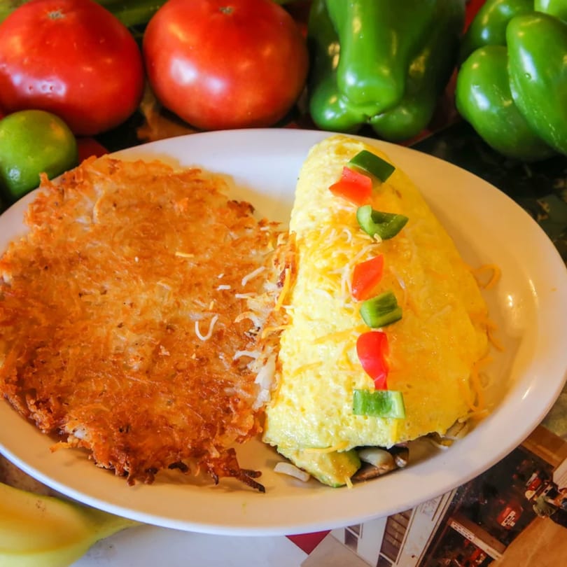 A breakfast plate with a golden-brown hash brown patty and a cheese omelet topped with bell peppers.