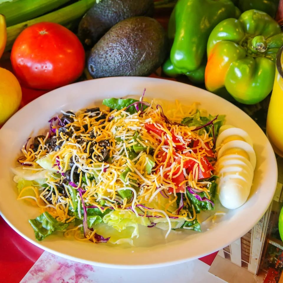 A fresh salad with lettuce, tomatoes, olives, shredded cheese, and sliced hard-boiled eggs.