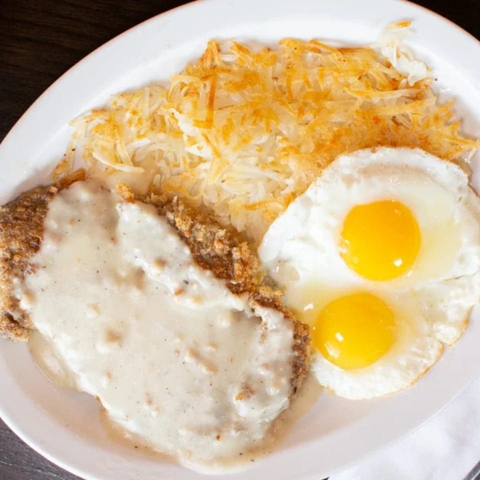 Chicken fried steak with gravy, hash browns, and two sunny-side-up eggs on a white plate.