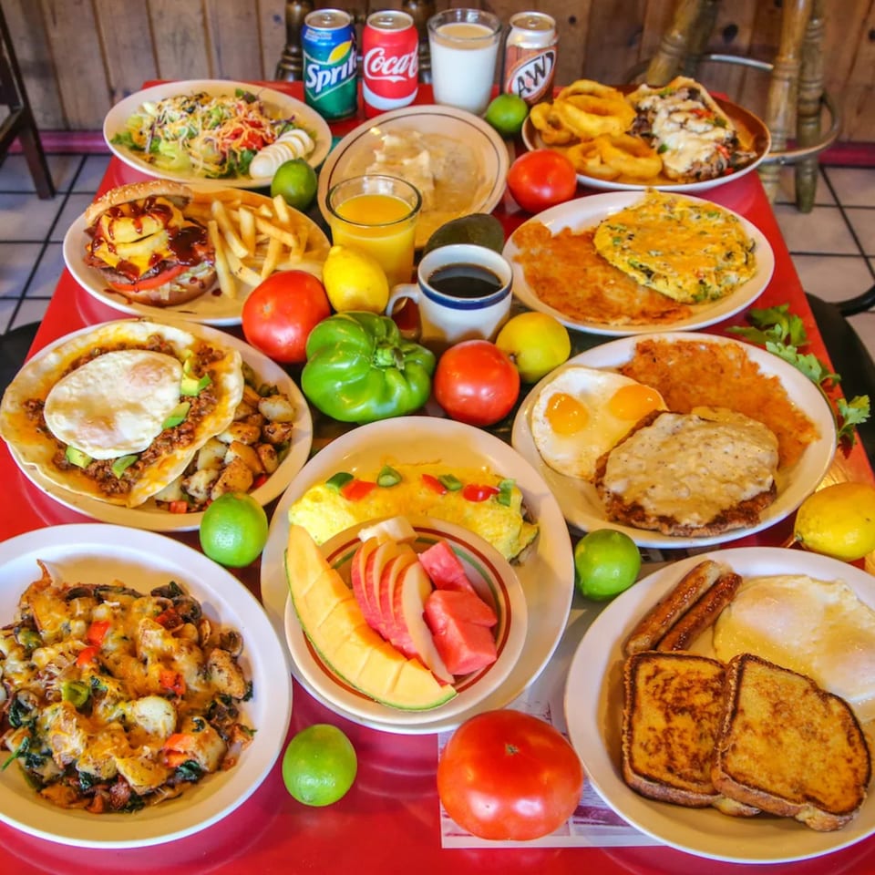 A red table laden with numerous plates of breakfast and lunch items, drinks, and fresh produce.